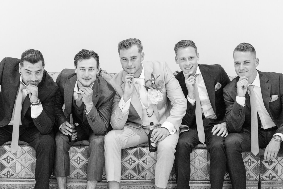 Groom Jochem sits on a Morroccan sofa posing with his groomsmen before the ceremony in a black and white photo