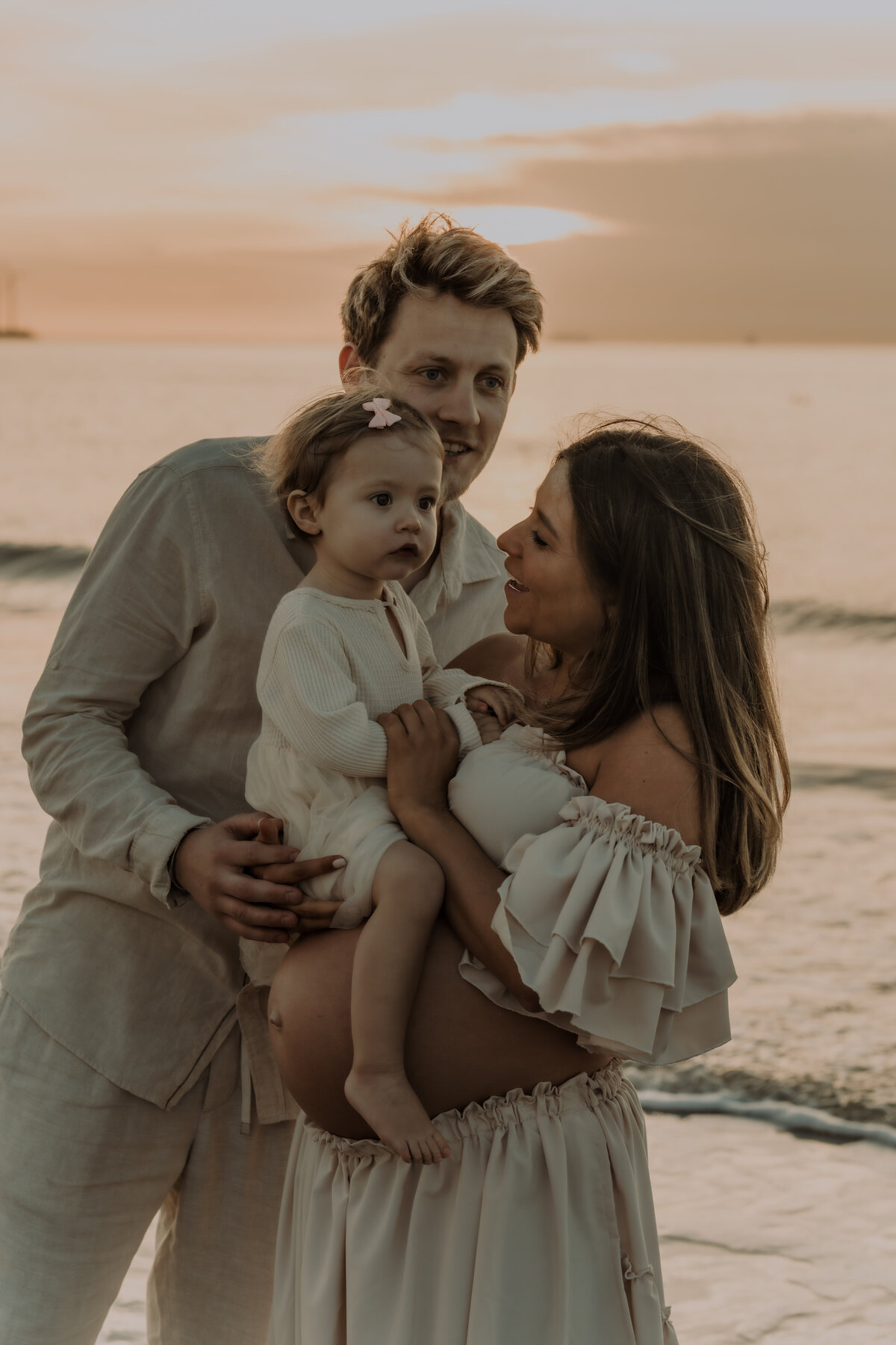 Gezin poseert voor zwangerschapsshoot op het strand tijdens zonsondergang