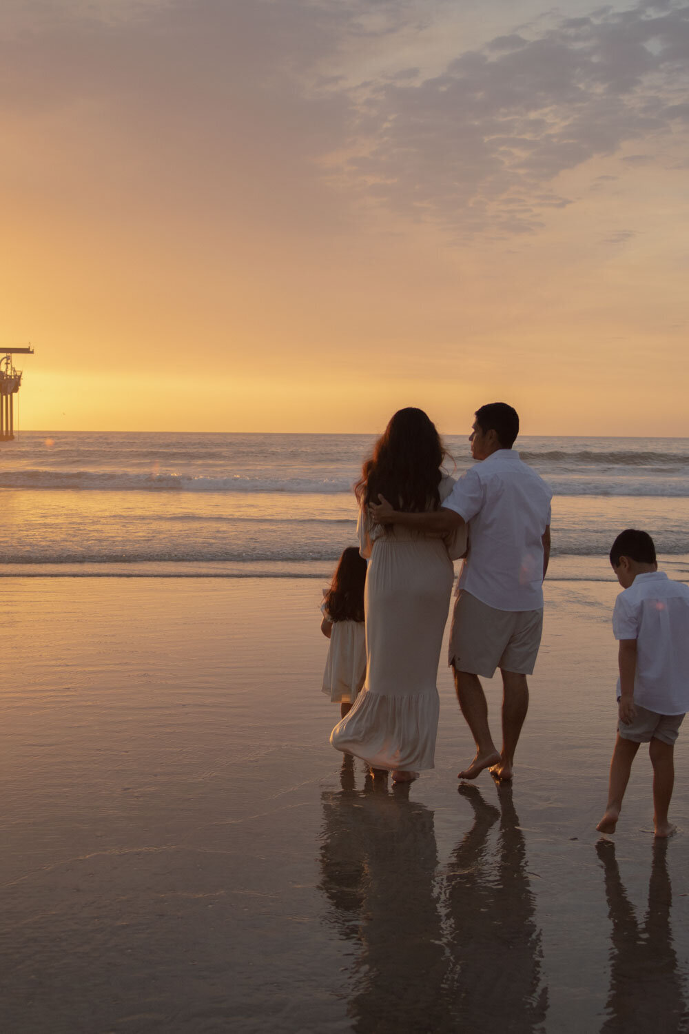 A family walking together along the shore, framed by a setting sun