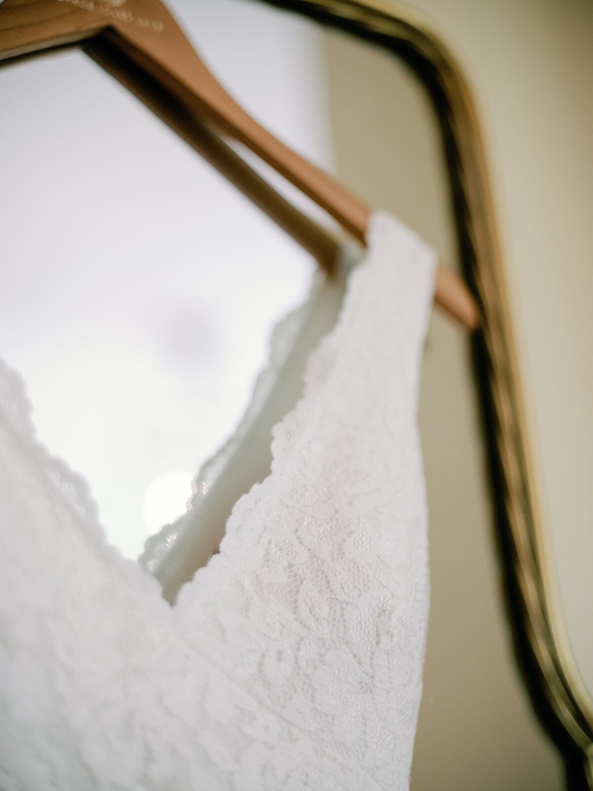 Closeup  of a wedding dress hanging on a mirror showcasing the lace texture.