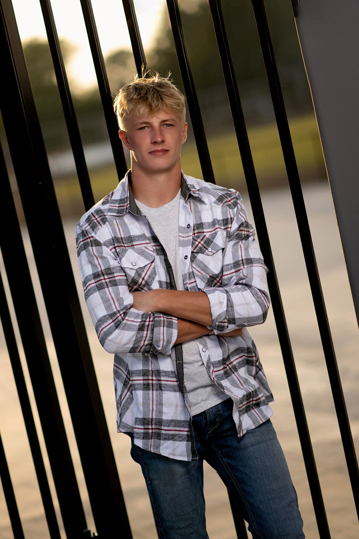 A Pella Senior Photography image of a high school senior leaning on metal gates at sunset in plaid and jeans