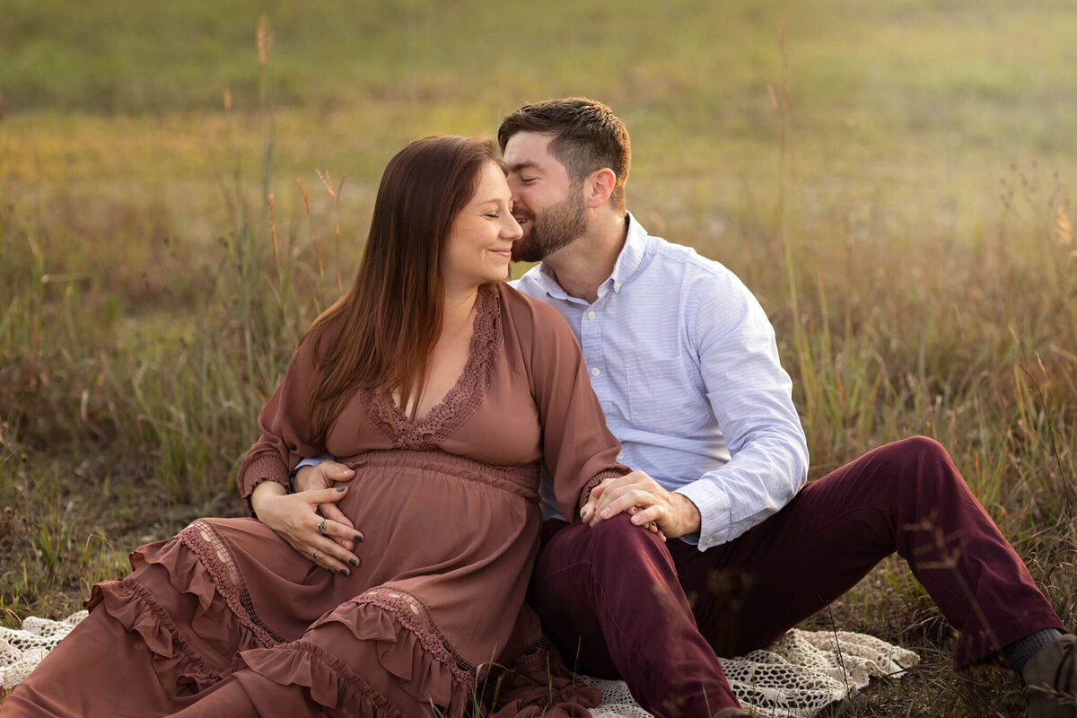 NJ Maternity photos of dad kissing mom on a blanket