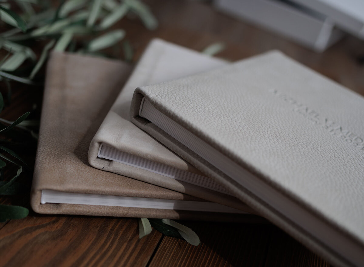 Three newborn and baby photography ablums stacked on one another. Two have suede leather covers and one has a fiine art linen cover