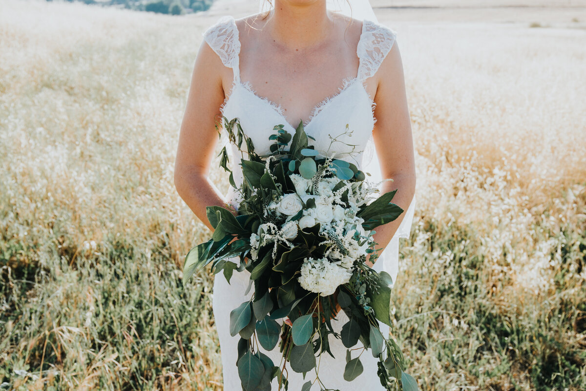 Bride stands in field holding bouquet and camera angle focuses from the neck down.