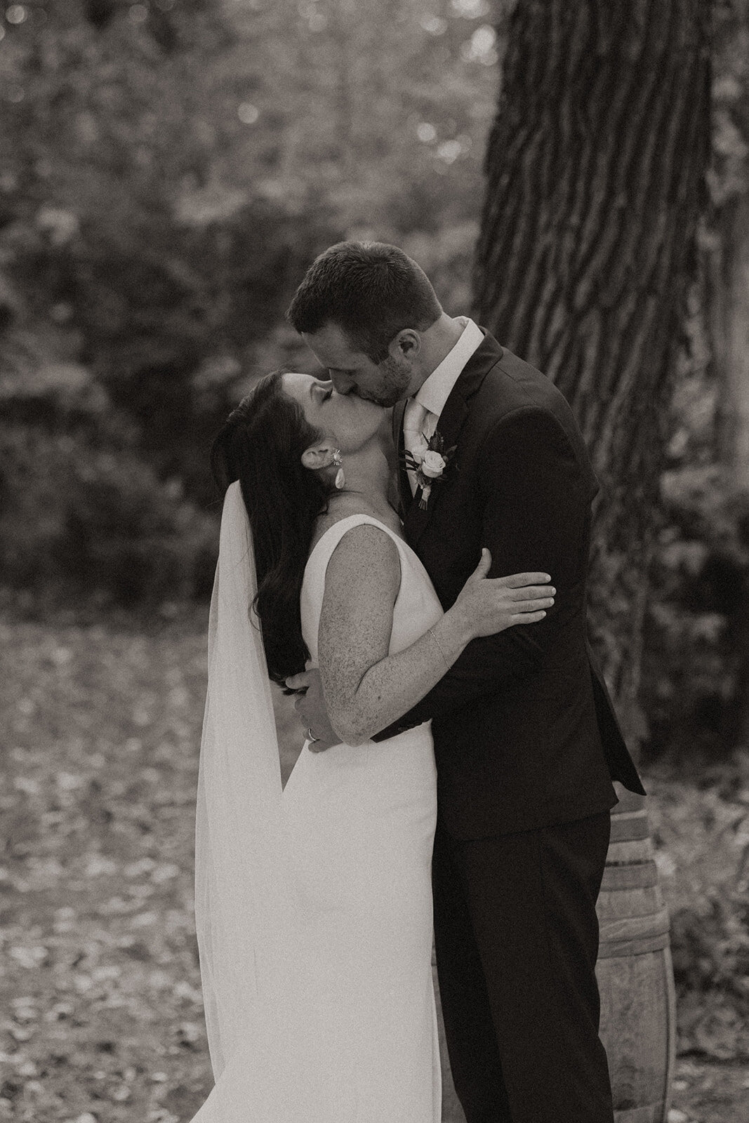 A bride and groom sharing a kiss, with the bride's hand on the groom's chest and a wooded area in the background at an Illinois wedding.