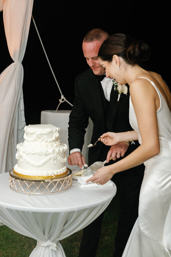 A joyful moment as the newlyweds share a laugh while cutting their elegant white wedding cake, decorated with pearl-like details. Captured by Claudia Amalia Photography, a Florida Keys wedding photographer specializing in destination wedding photography.
