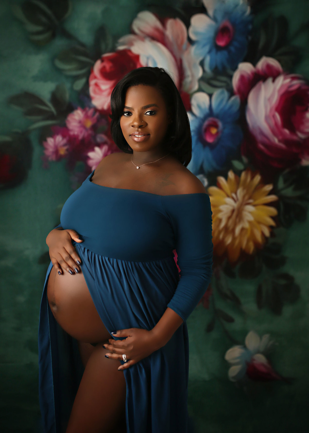 gorgeous pregnant mother in blue maternity dress belly exposed standing against floral print backdrop