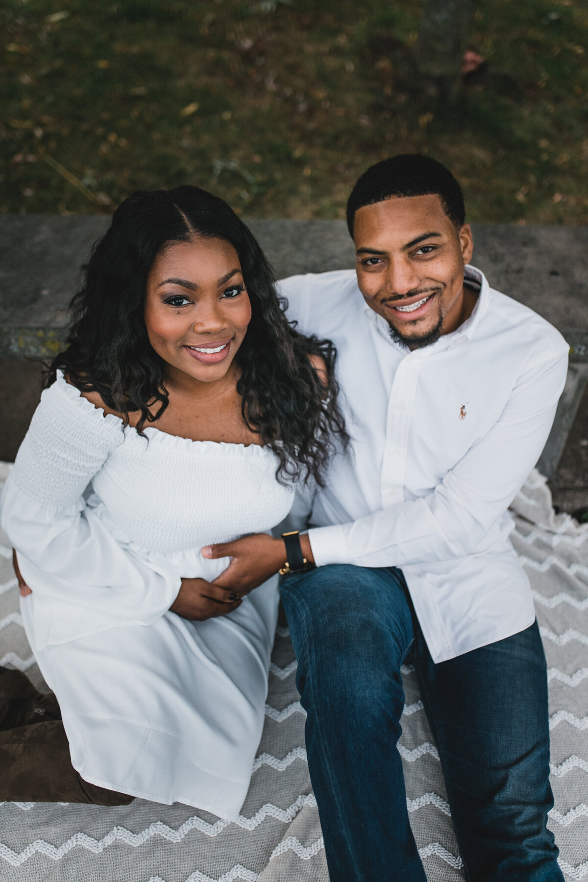 Pregnancy announcement photo with woman and man sittings on a blanket outside.