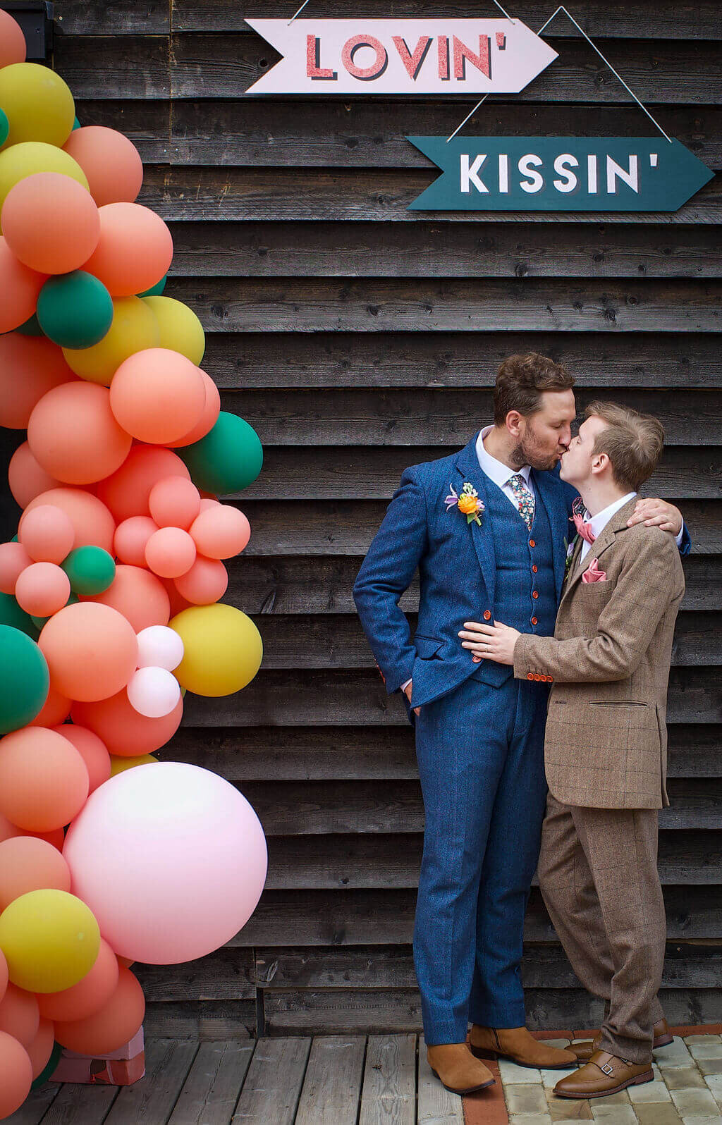Groom and groom kissing in front of balloons at The Canary Shed Essex