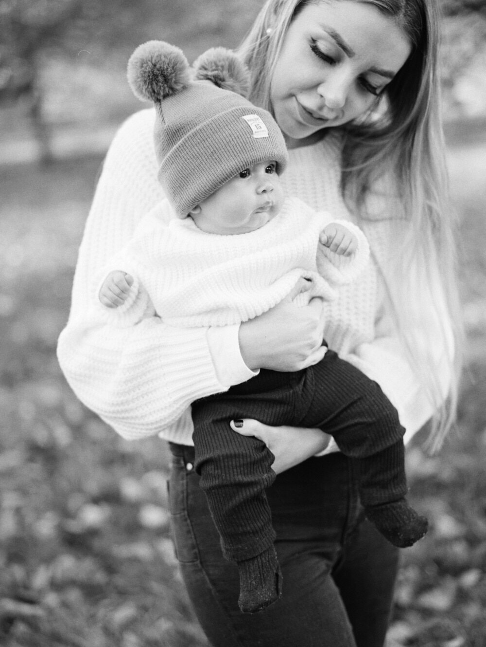 baby girl wearing pom pom beanie, young mother holding daughter on hands