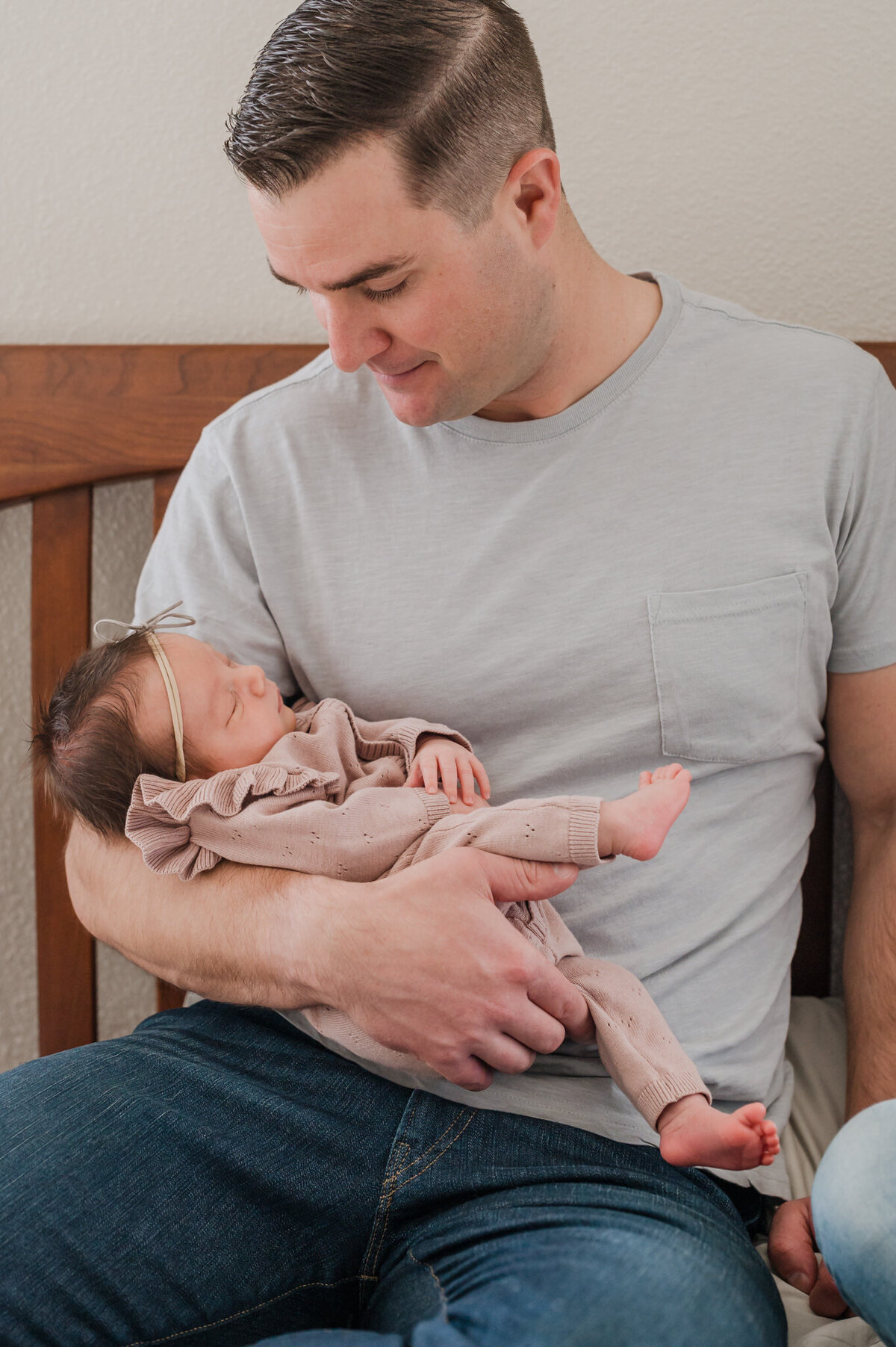 Dad cradles his baby daughter and gazes down at her during in-home newborn pictures in San Antonio.