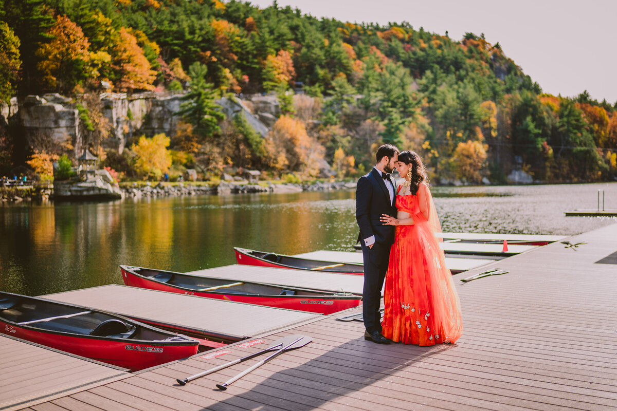 An indian bride and groom standing near the boating docks in traditional fall-colored orange indian lehnga at mohonk mountain house in new paltz