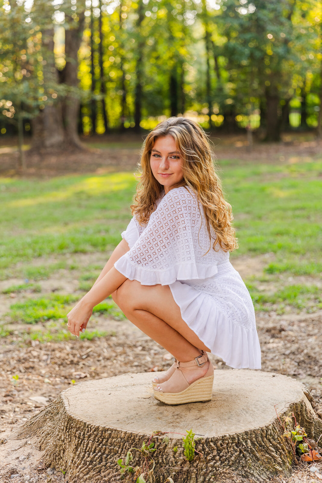 wide shot senior girl squadding down and looking at the camera over her shoulder in an Atlanta park during portrait photoshoot