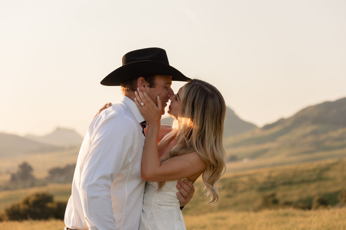 Candid couple kissing during engagement photos in golden hour field with mountains in San Luis Obispo 
