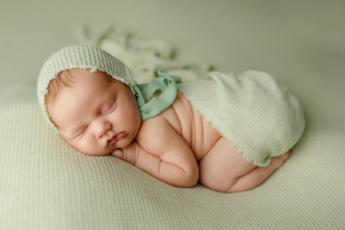 Newborn baby posed on a sage green knit blanket, wearing a matching bonnet and sleepy bloomers during their studio session. Captured by Inland Empire newborn photographer Kaitlyn Dawn Photography.