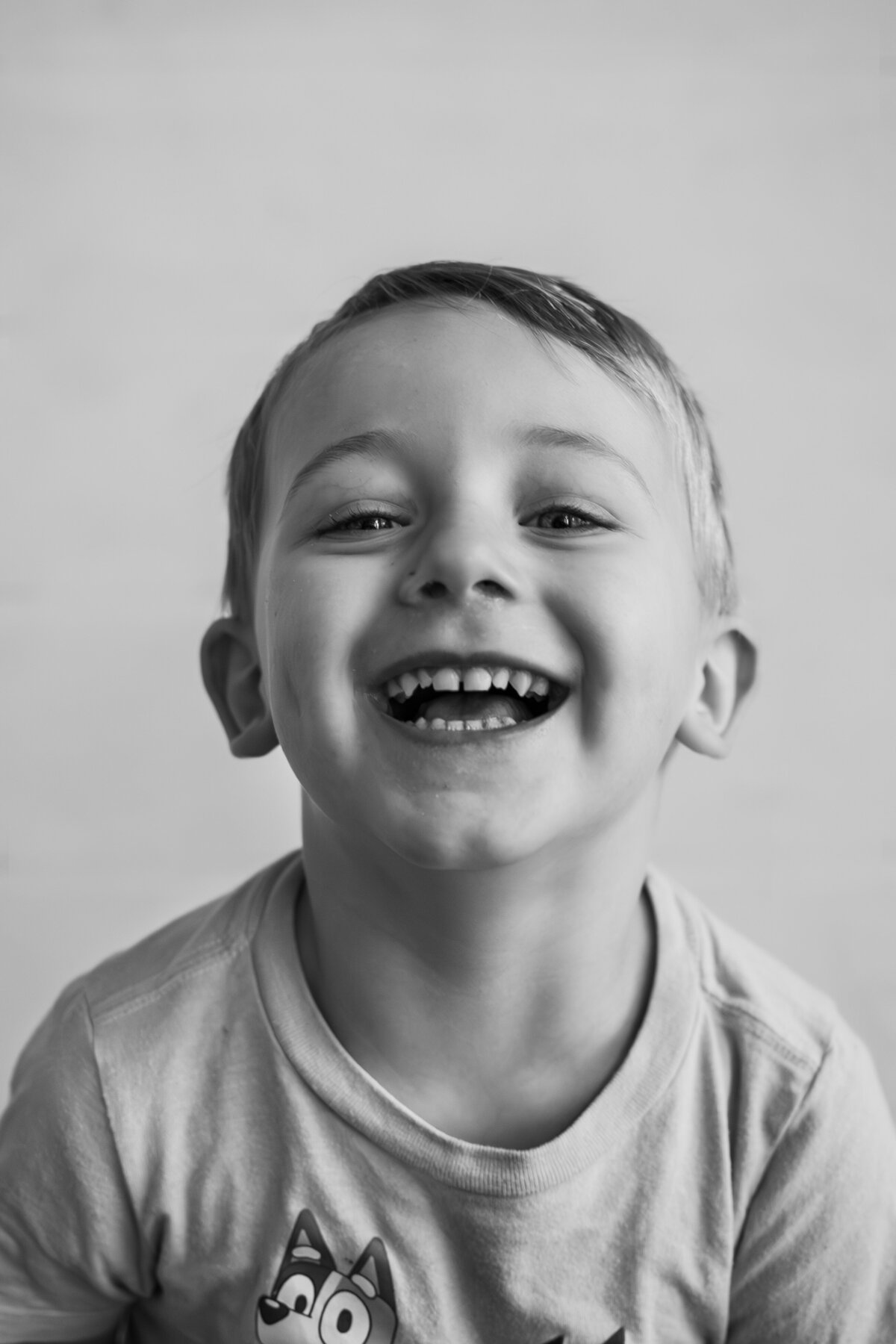 Black and white photo of toddler boy wearing a Bluey shirt smiling at the camera.