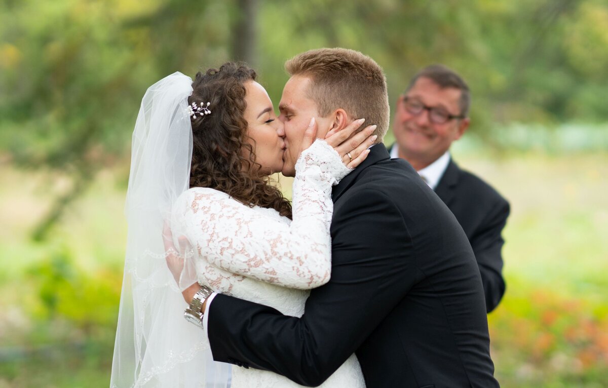 A close-up of the bride and groom sharing a tender kiss, capturing the intimate and affectionate moment between them. The focus is on their loving connection and the joy of their wedding day, showcasing their closeness and happiness in a beautiful, romantic setting.