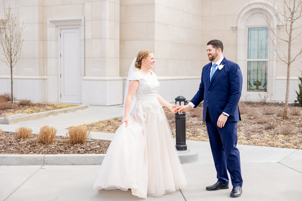 Bride smiling at her groom as they hold hands outside the Taylorsville Utah Temple.