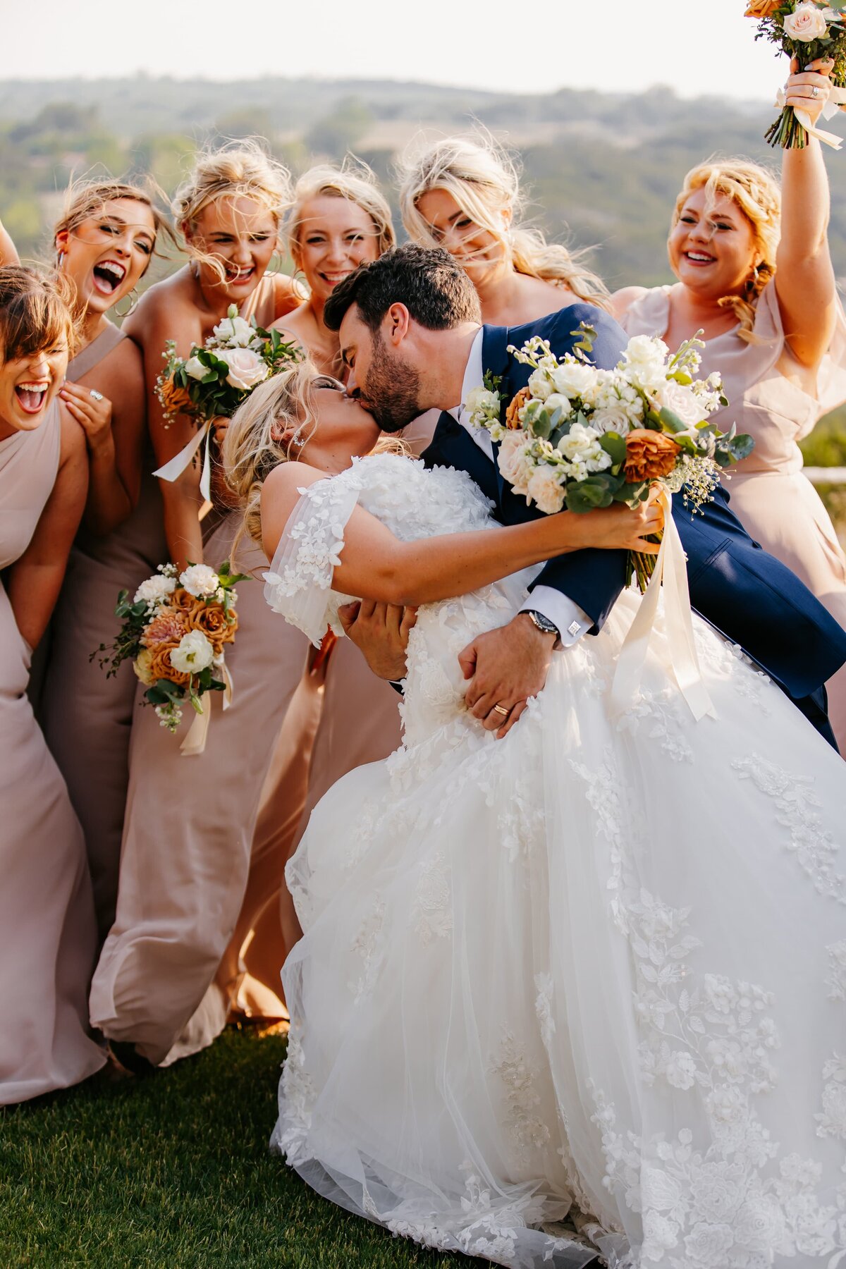 groom dips bride in a kiss surrounded by cheering bridesmaids