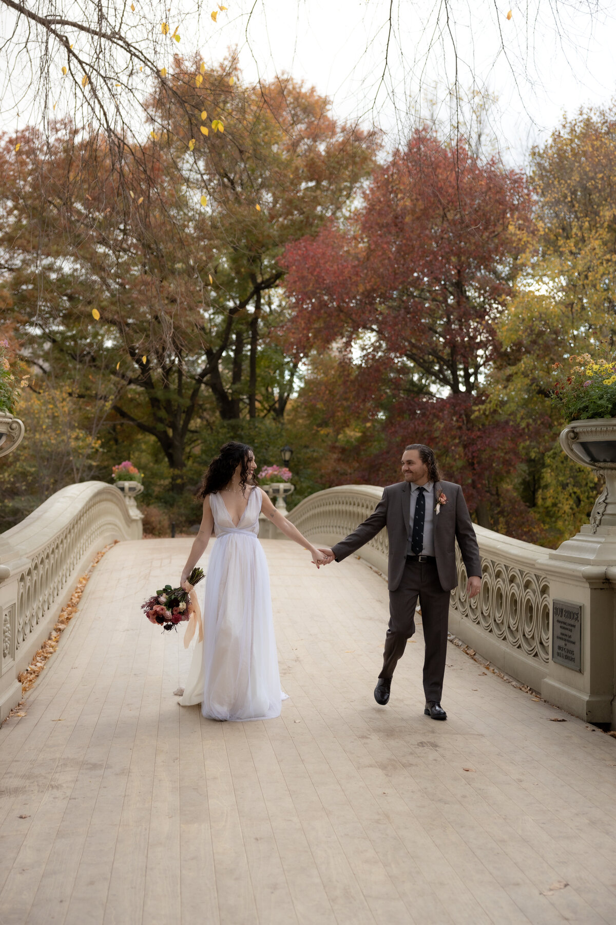 The couple holding hands and smiling as they walk through a peaceful Central Park path.