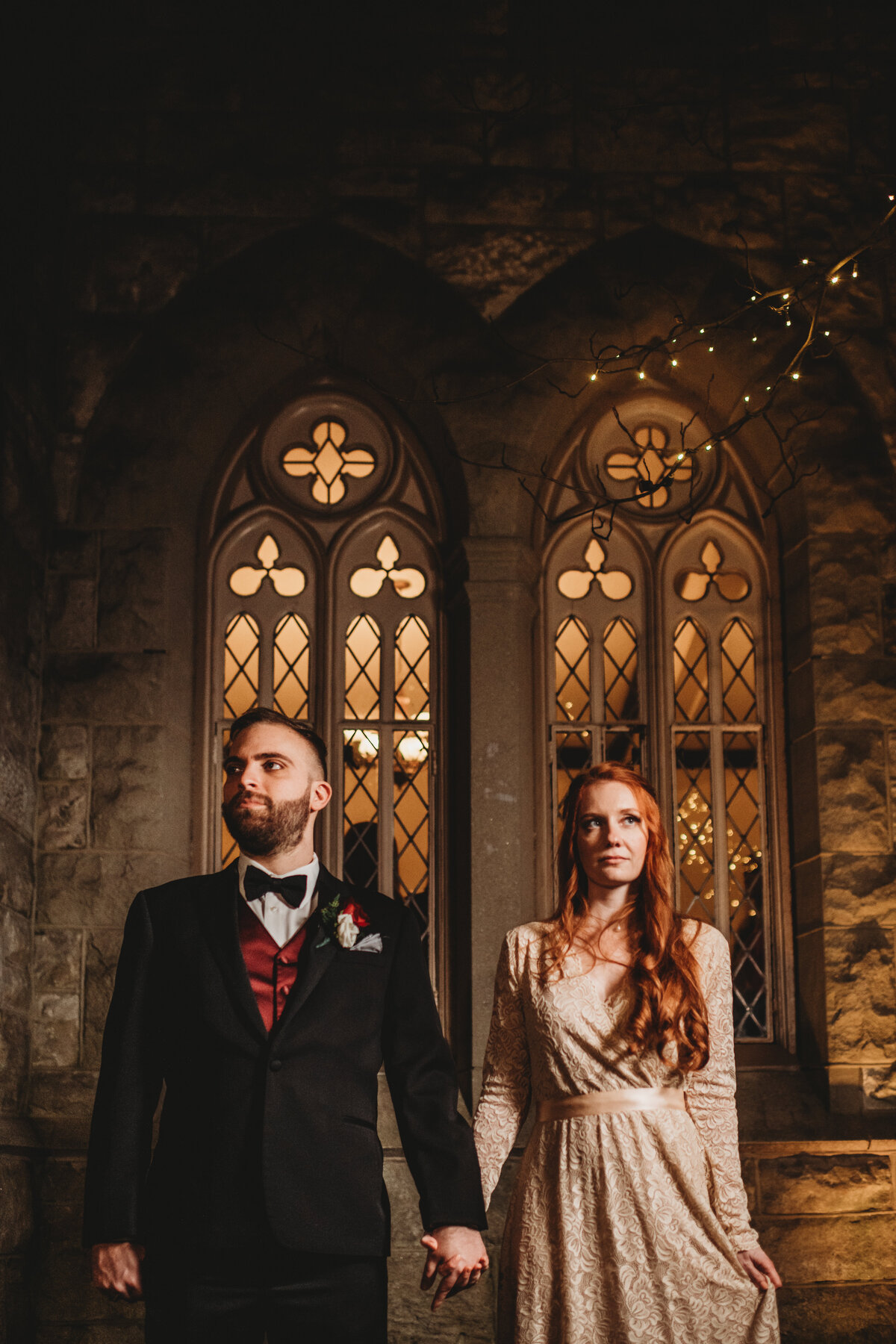 Bride and groom holding hands and standing in front of large glass windows in a chapel made of stone for their Baltimore wedding