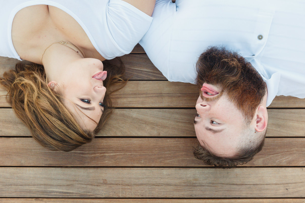 Engaged couple laying down sticking tongue out at each other