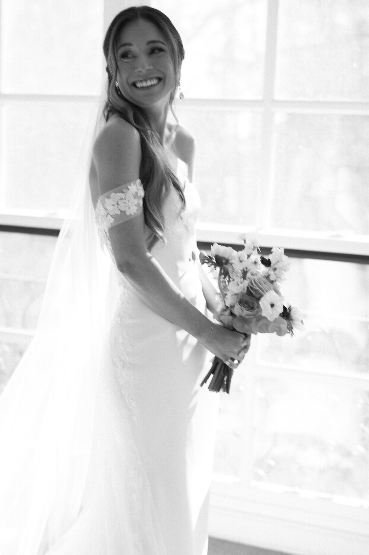 Bride holds her bouquet in front of a window 