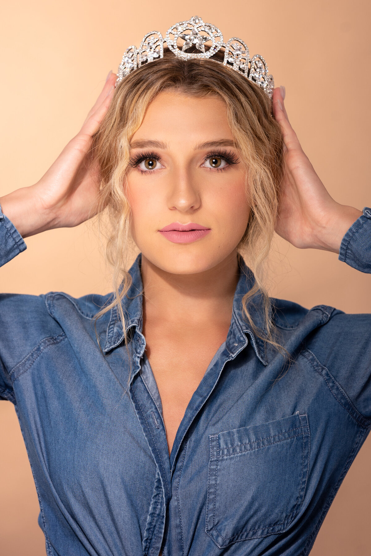 Miss teen Austin wearing a crown looking straight to the camera and holding her crown with two hands