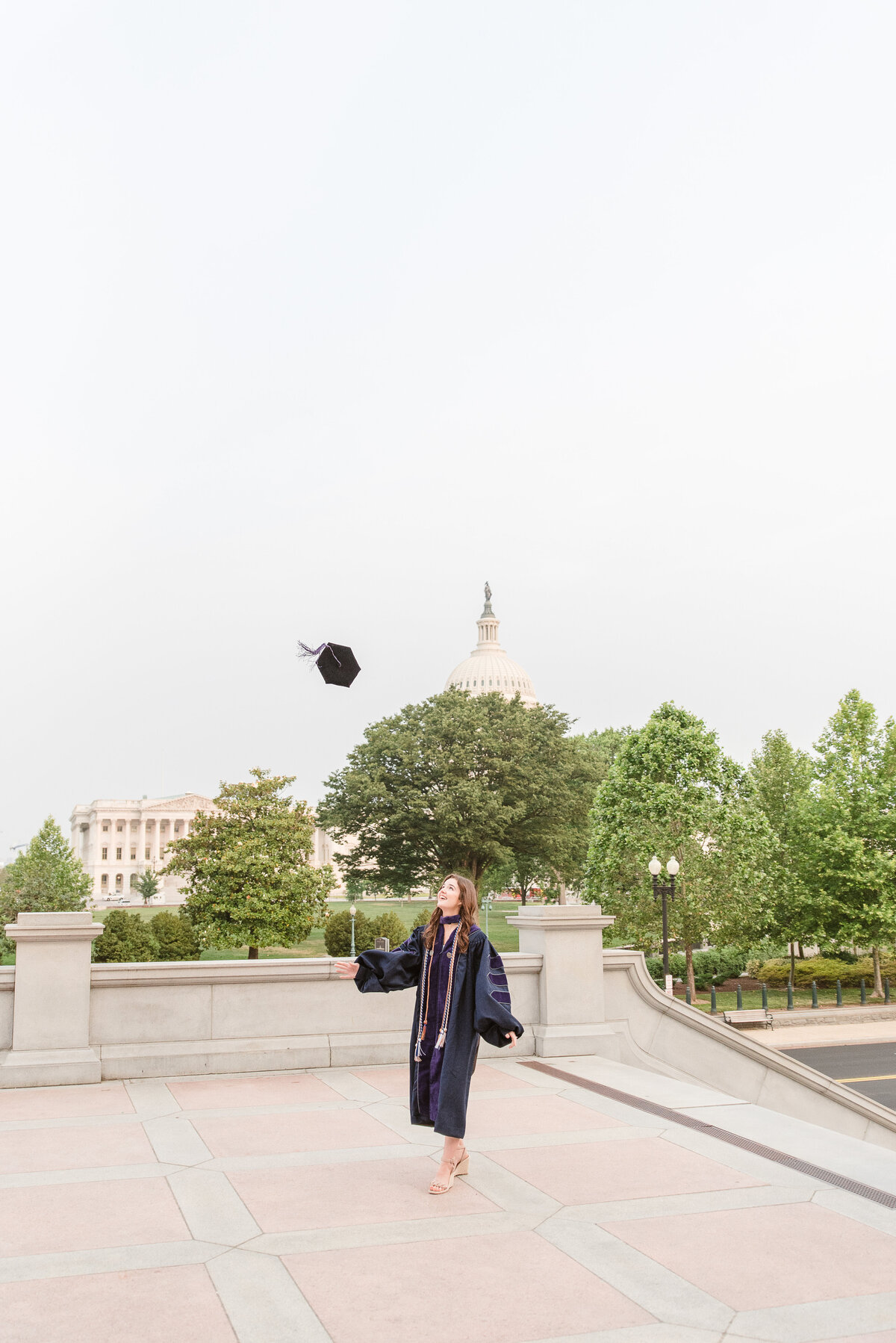 grad throwing cap in the air with capitol behind her