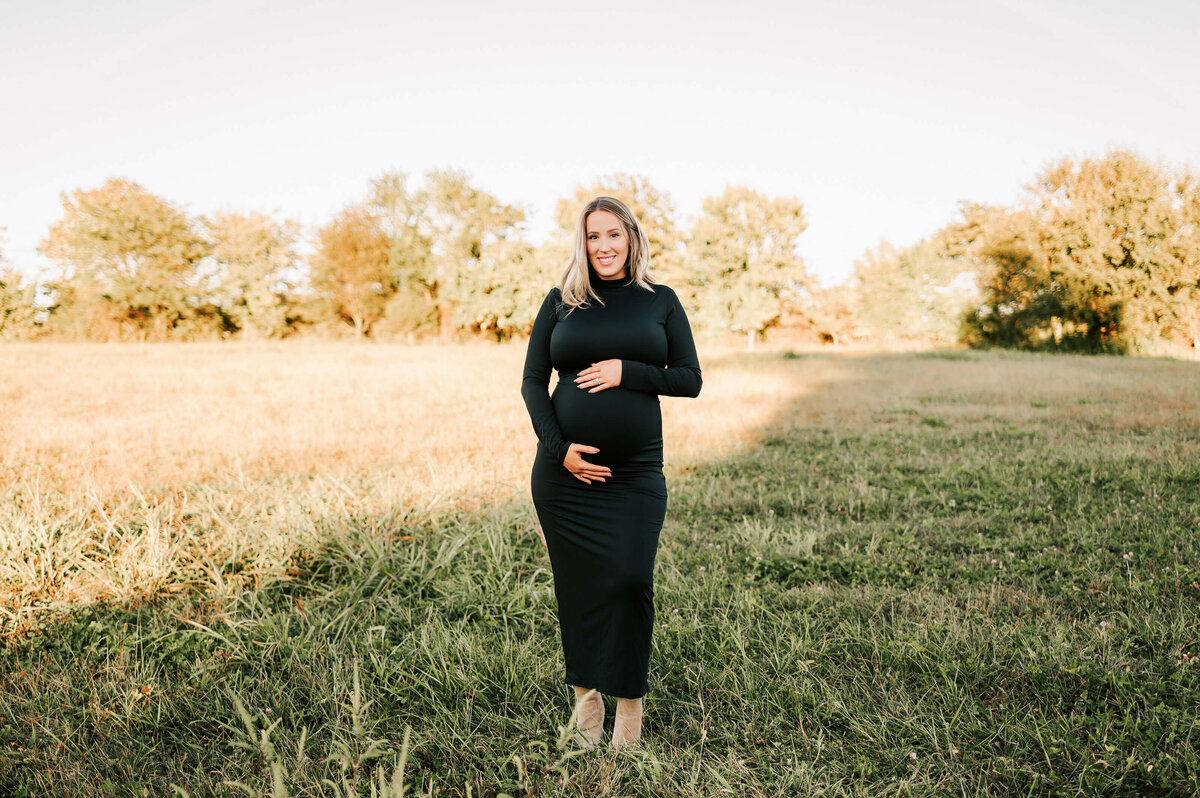 Springfield MO maternity photography of pregnant mom in black dress smiling in field