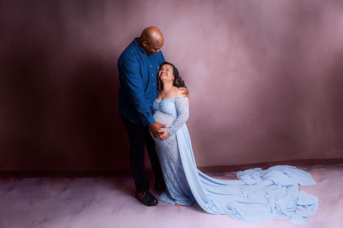  A pregnant woman in a blue dress stands beside a man, both smiling in a warm, joyful moment in Youngstown, Ohio