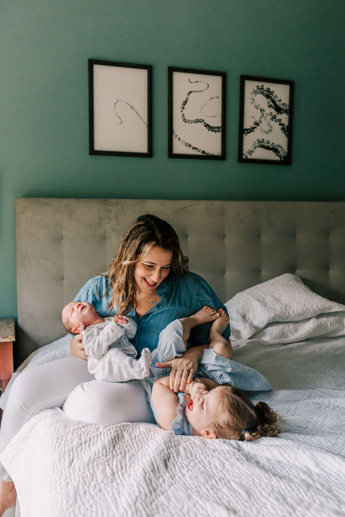 A mother tickling her toddler girl while holding her newborn son