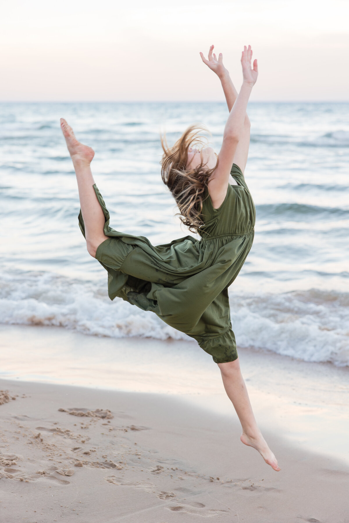 A little girl in a green dress is dancing along the beach