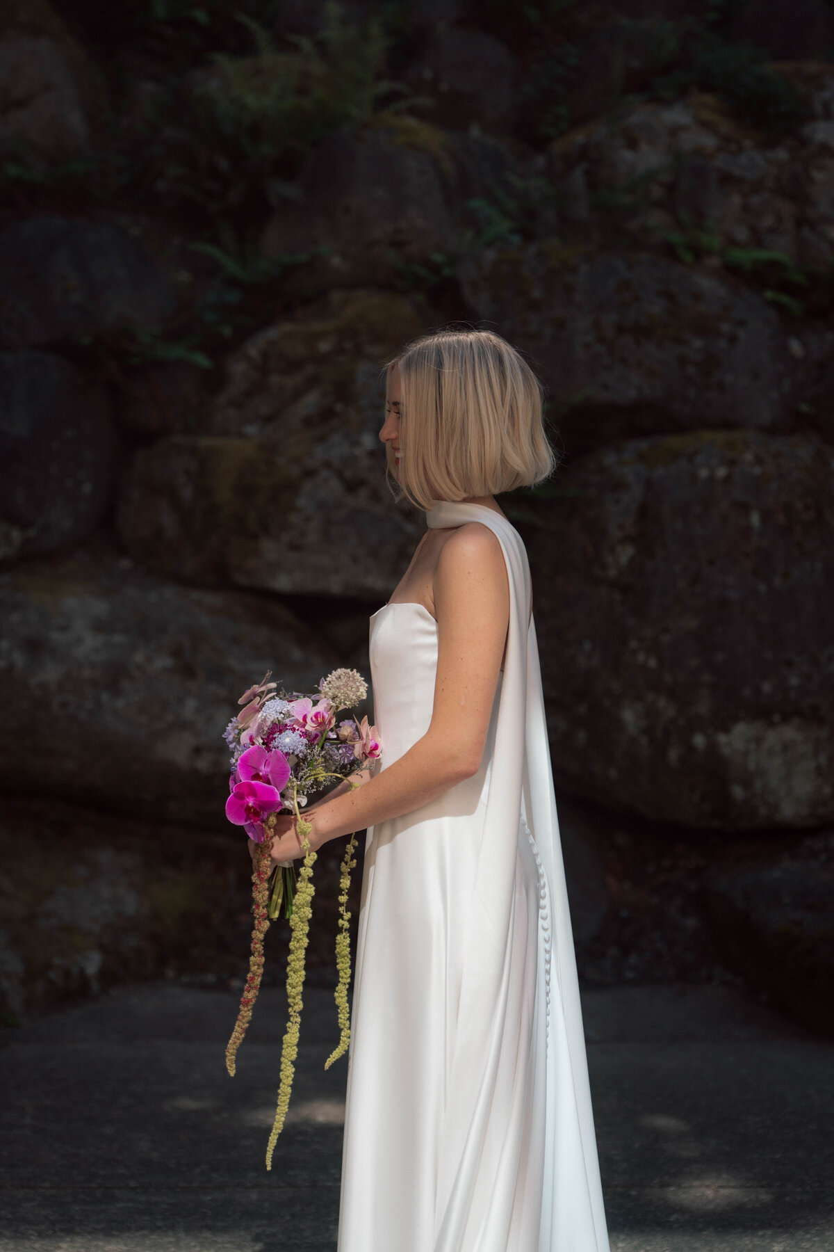 Blonde bride holding colorful bouquet in front of natural stone wall