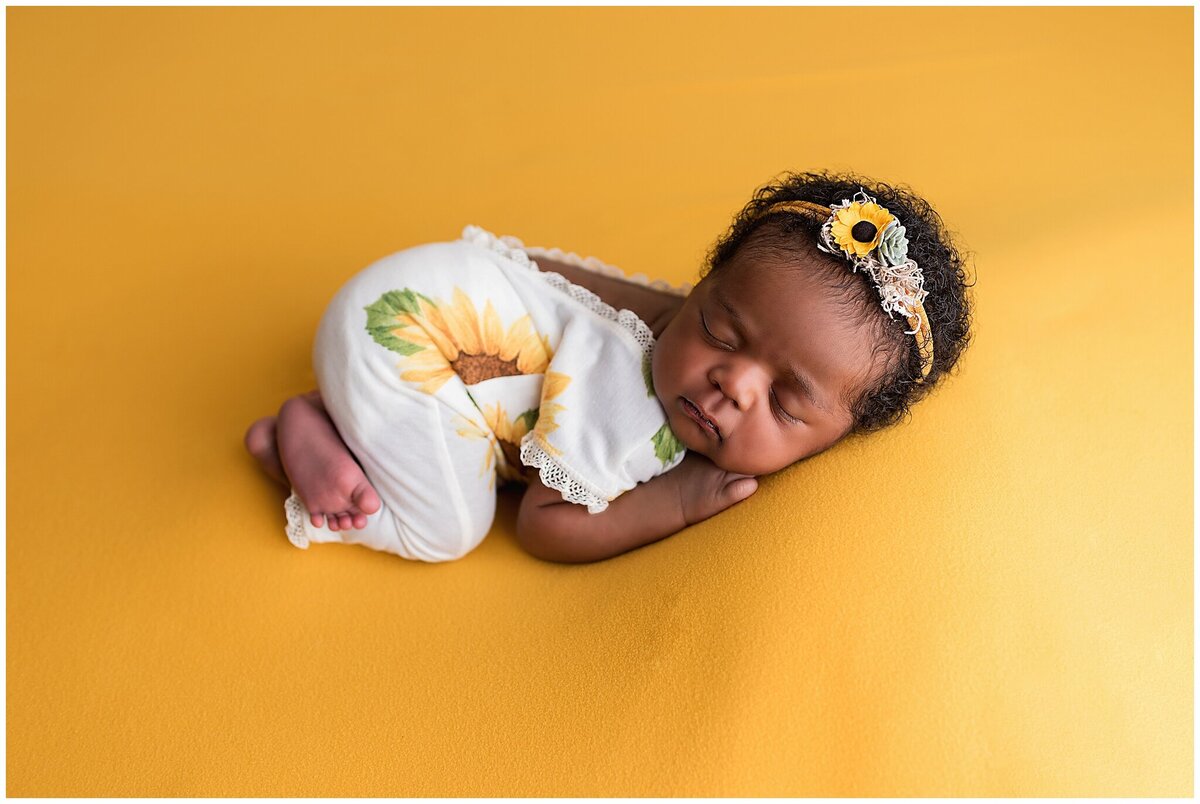 newborn wearing sunflower outfit posed on mustard backdrop