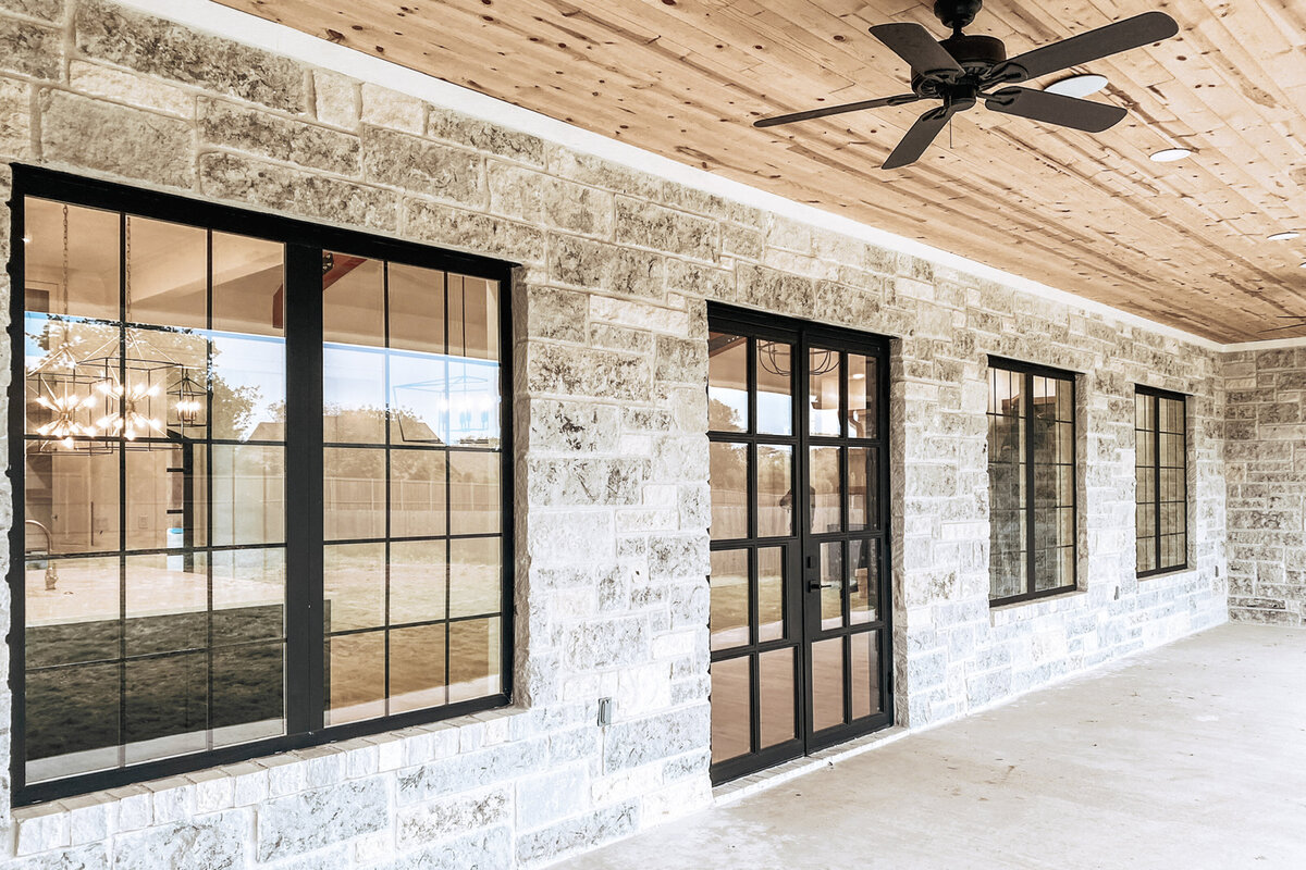 back porch of home with limestone walls, black windows and wood ceiling