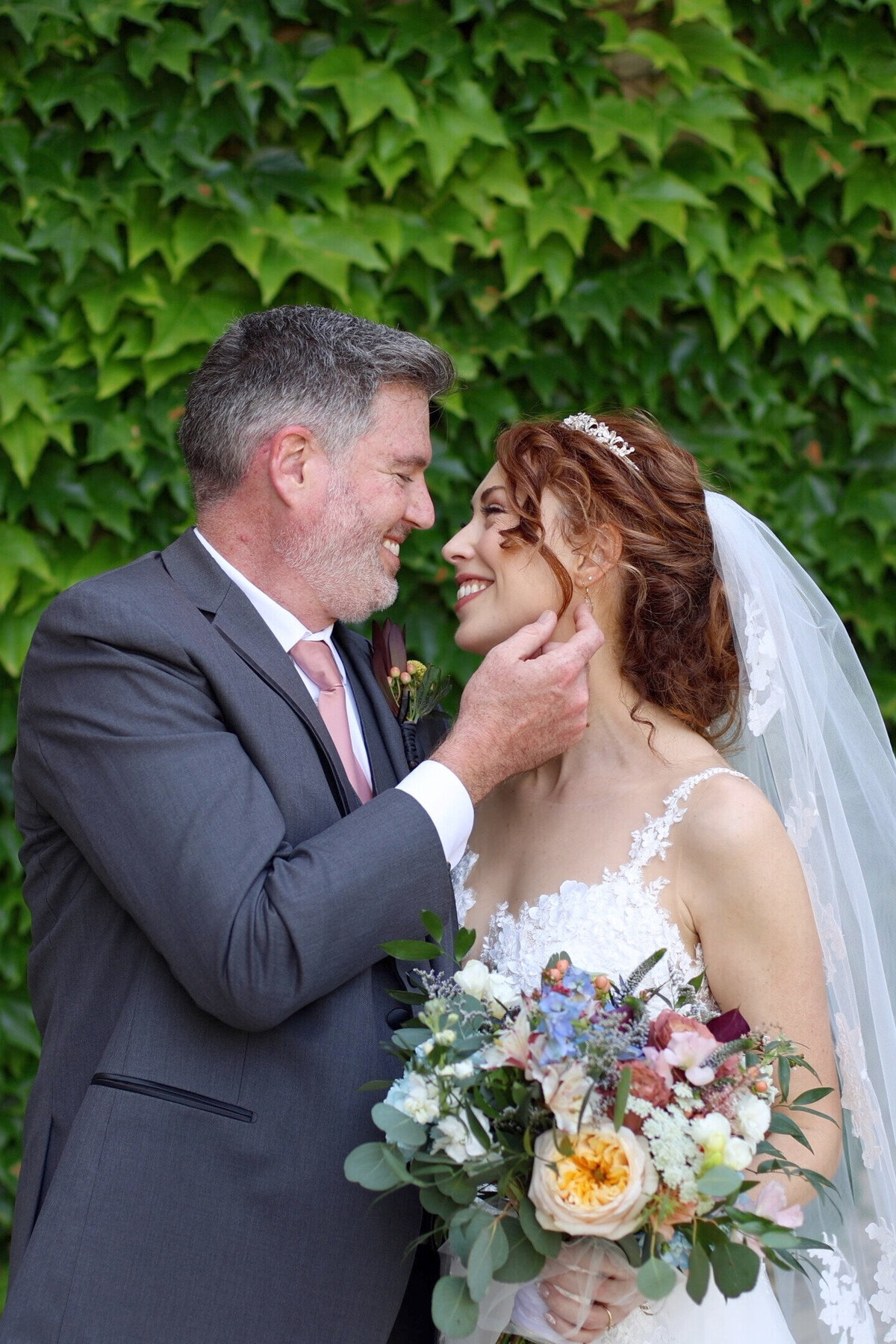 Groom touching brides cheek in front of greenery wall at Nelson Atkins Museum