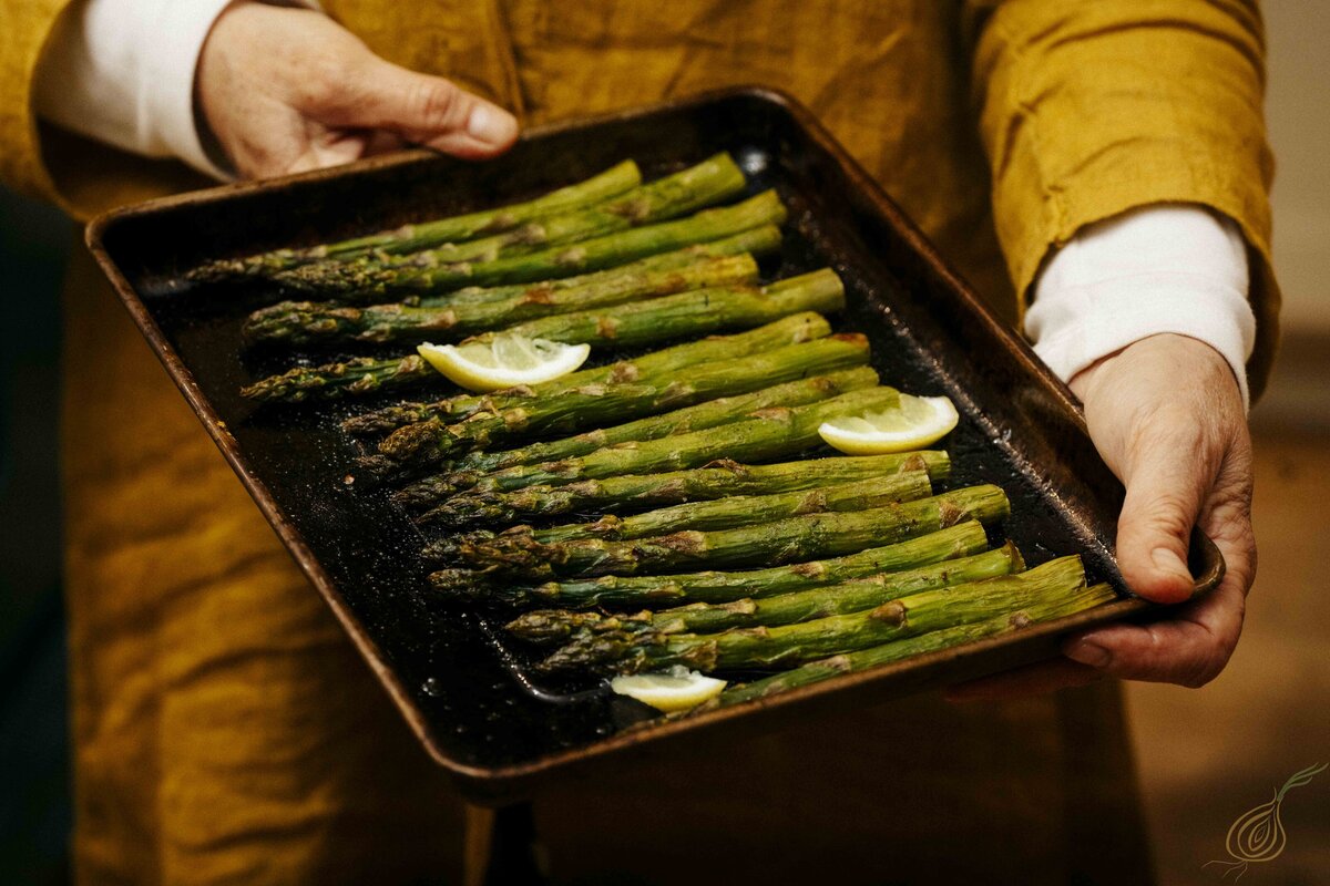 A person displaying a tray of asparagus accompanied by lemon wedges, emphasizing a fresh and nutritious meal option.