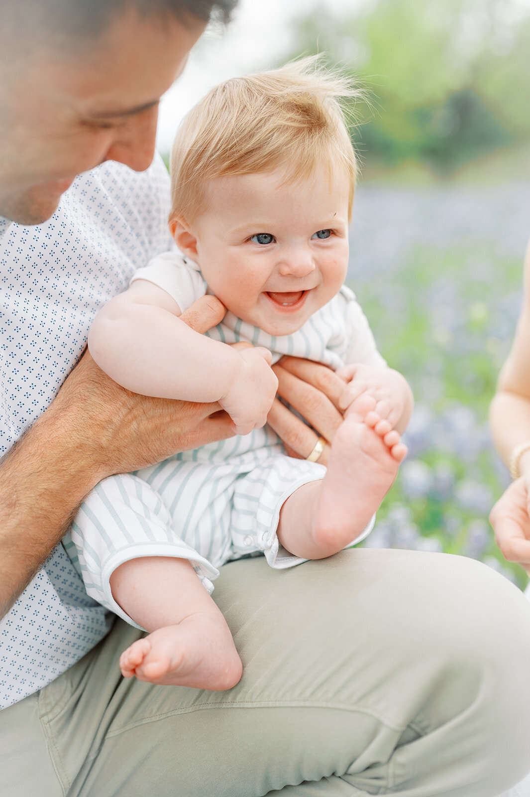 Little boy in classic children's clothing sitting in fathers lap surrounded by bluebonnets