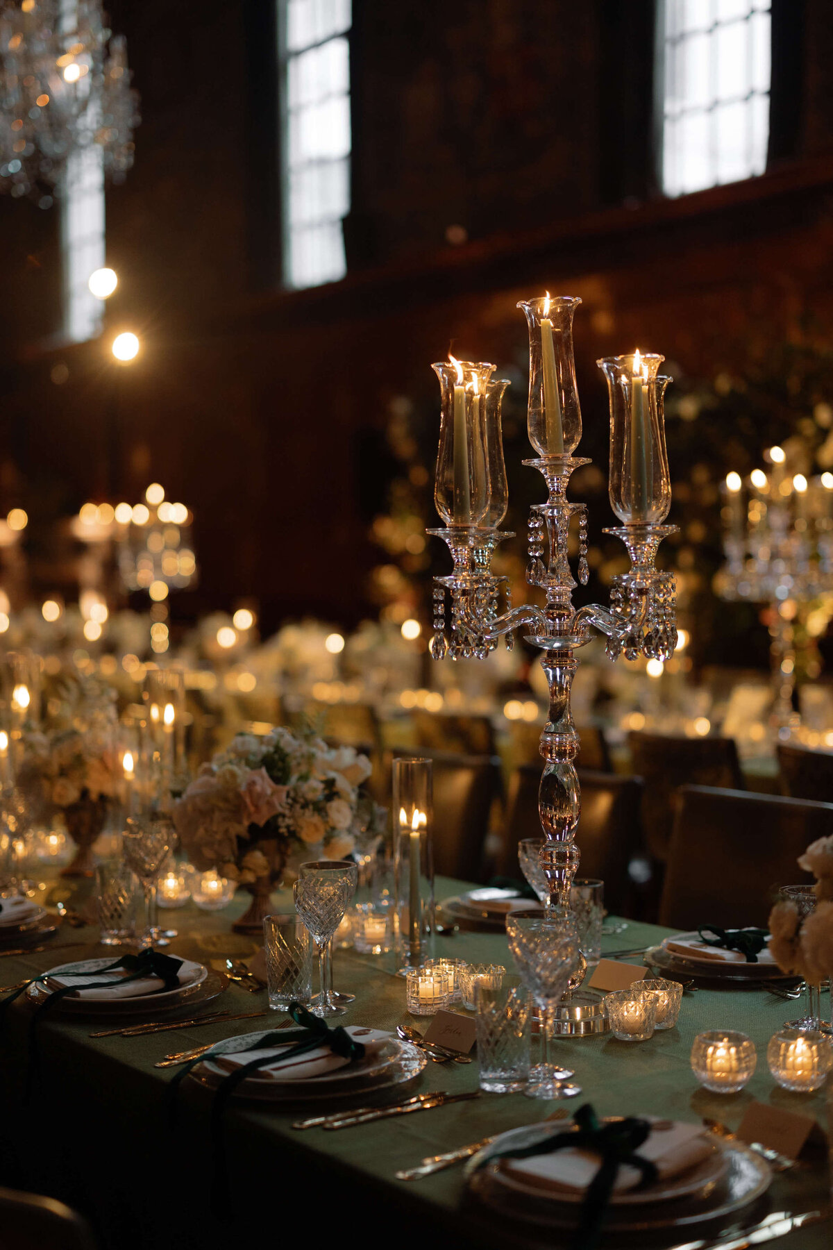 a candlelit wedding dinner at the ned london with tall crystal candelabras displayed on long tables of green linen and napkins tied with green velvet bows