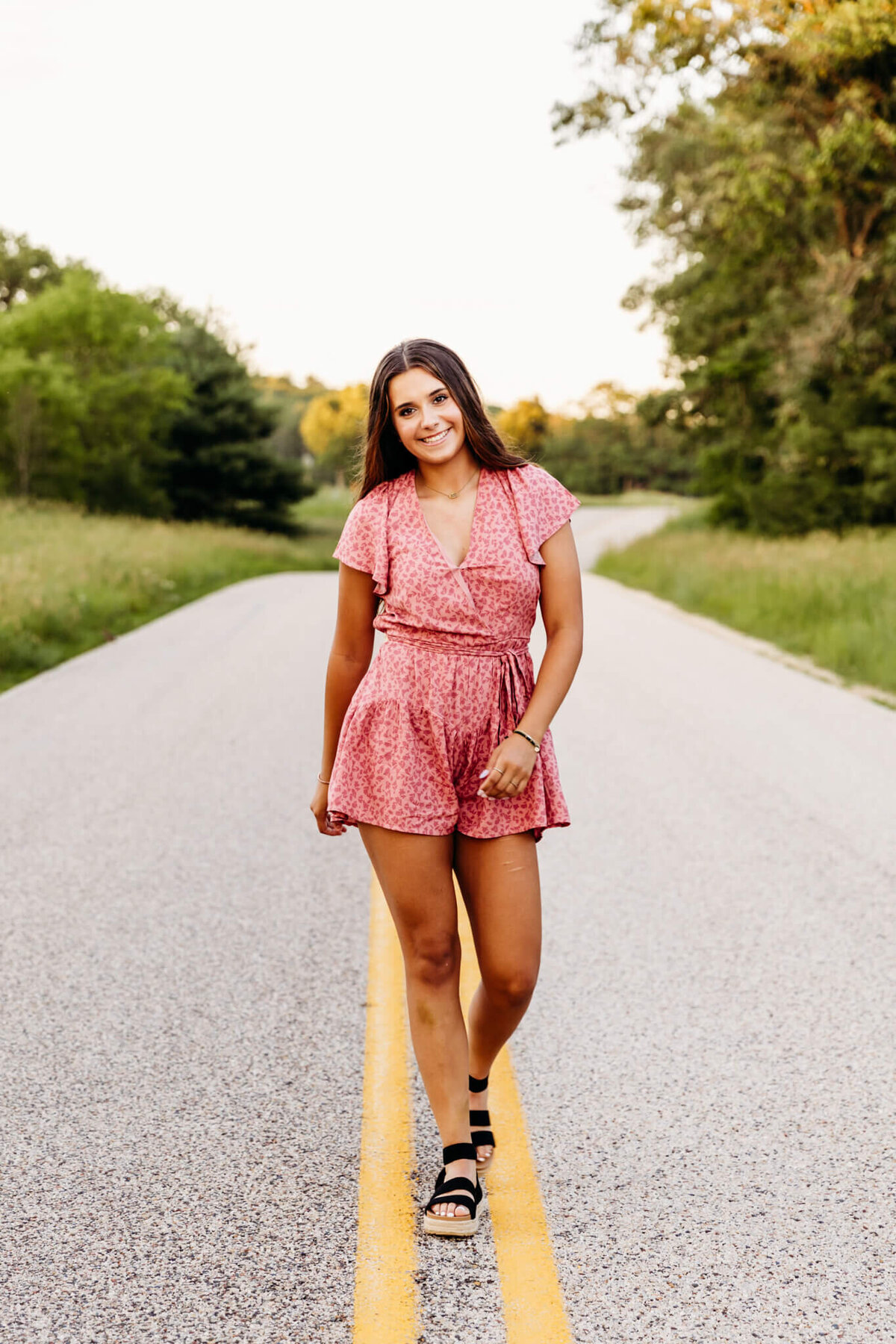 young lady walking on the yellow lines on a back road and smiling 