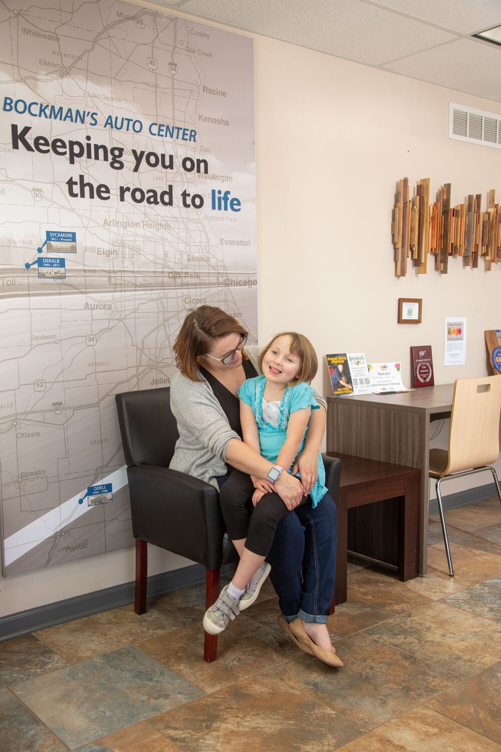 A woman and child are sitting in front of a wall that says keeping you on the road to life