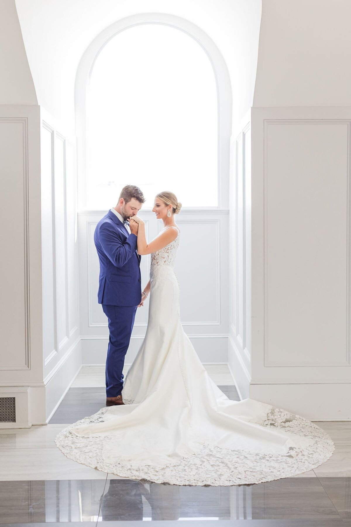 Groom kissing bride's hand in a white archway