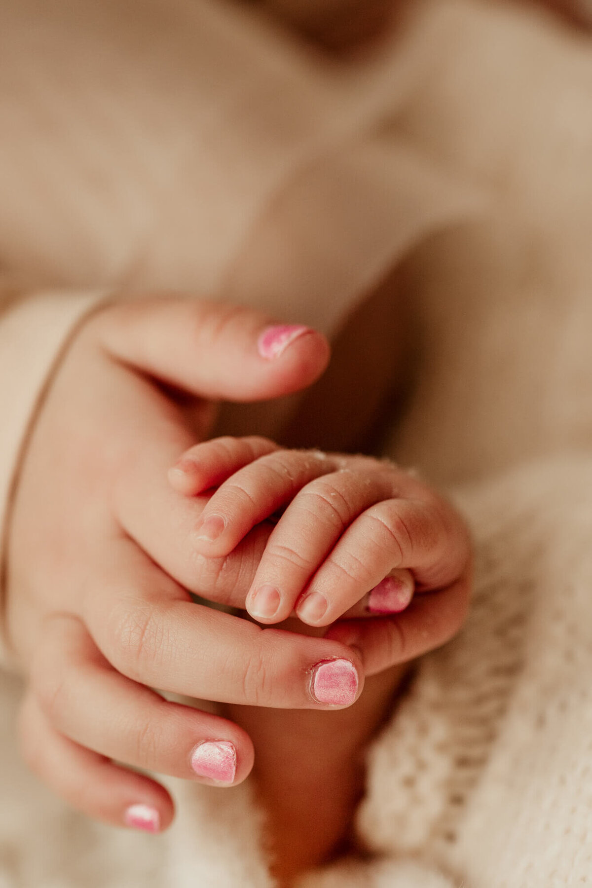 Big sister holds her tiny baby brother's hand in hers.
