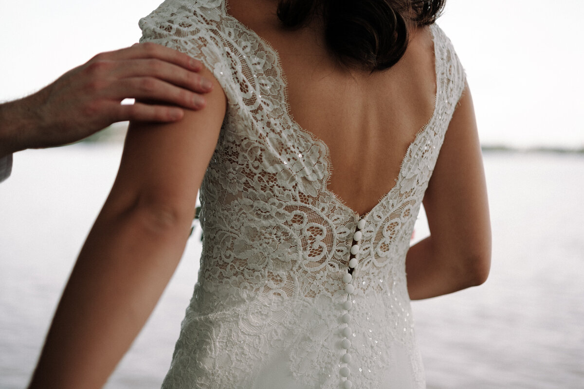 soft touch from her husband  overlooking the water with details of her dress