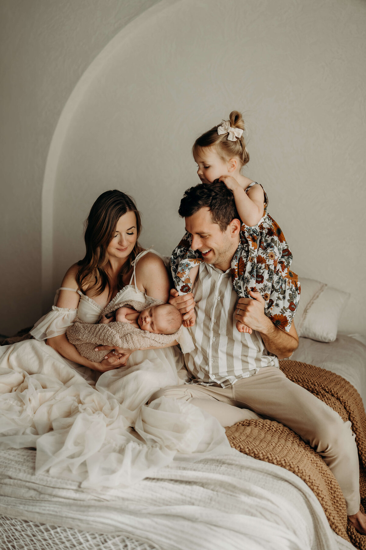 family of 4 poses on  a bed wearing a neutral wardrobe during a studio session in denver colorado