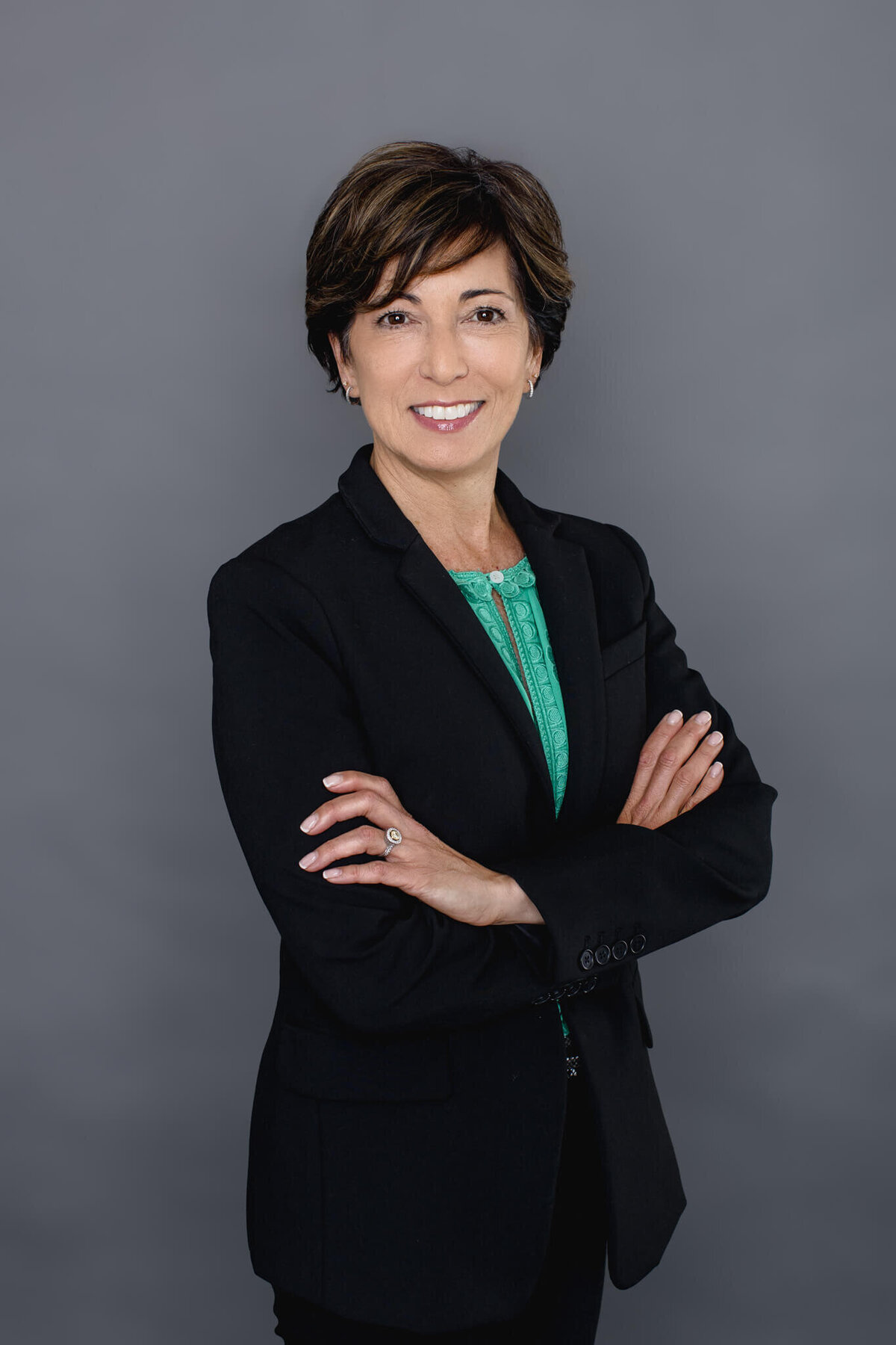 A woman with short black hair standing against a gray backdrop with her arms folded smiling at the camera