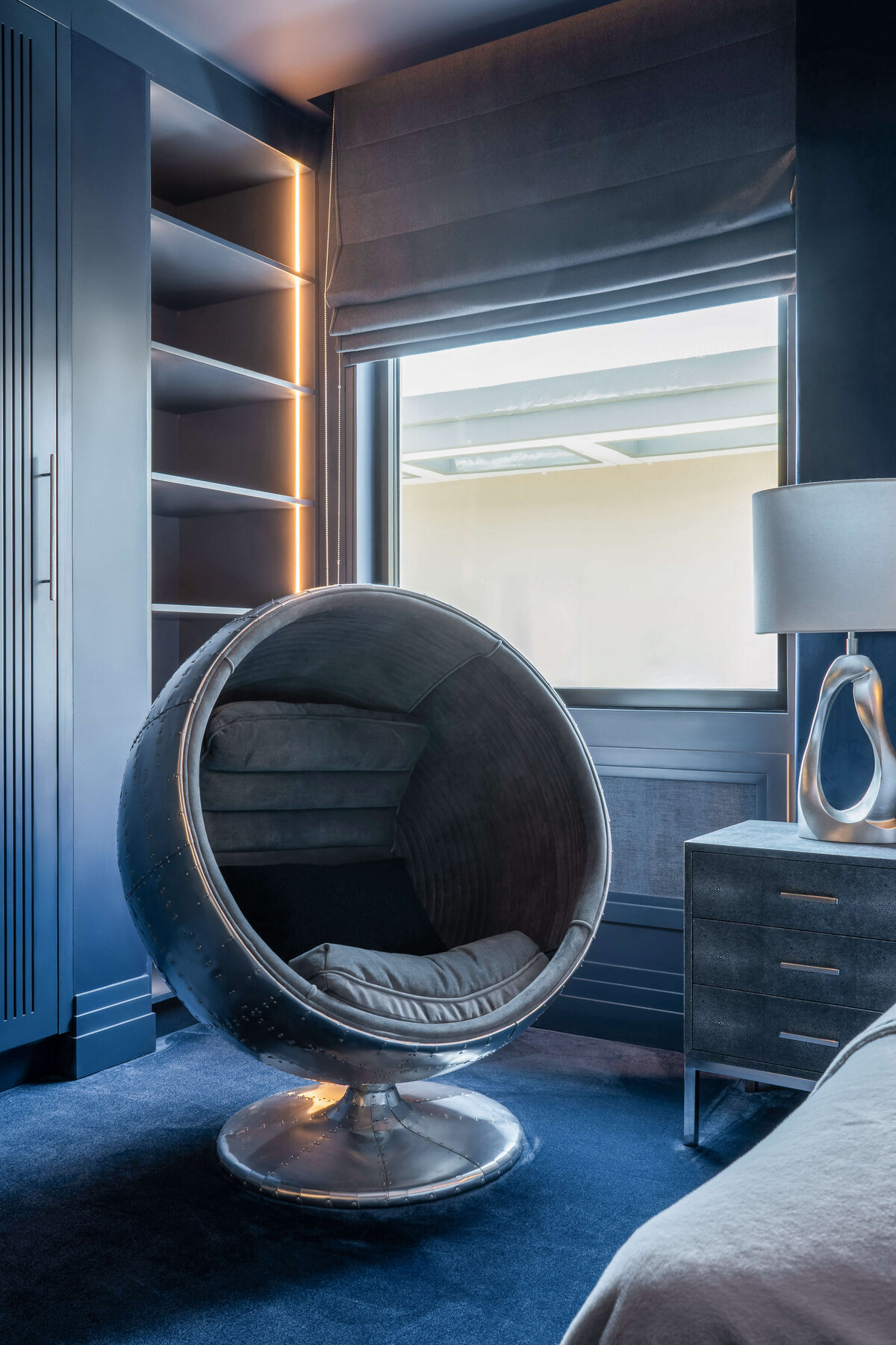 Chrome swivel ball chair with grey cushions in a boy'd blue oter space themed bedroom with blue carpet and walls.