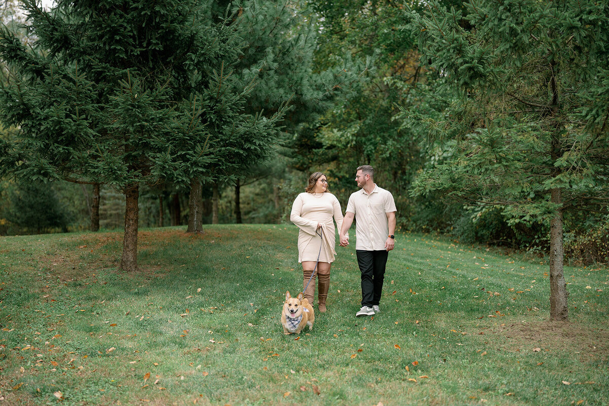 Couple walking with their dog through a grove of trees during their engagement session in Kalamazoo, Michigan.