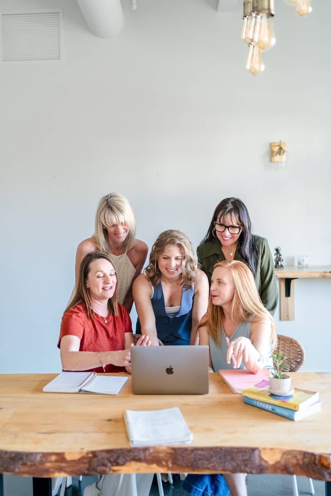 group of female entrepreneurs gathered around laptop smiling and working for brand shoot